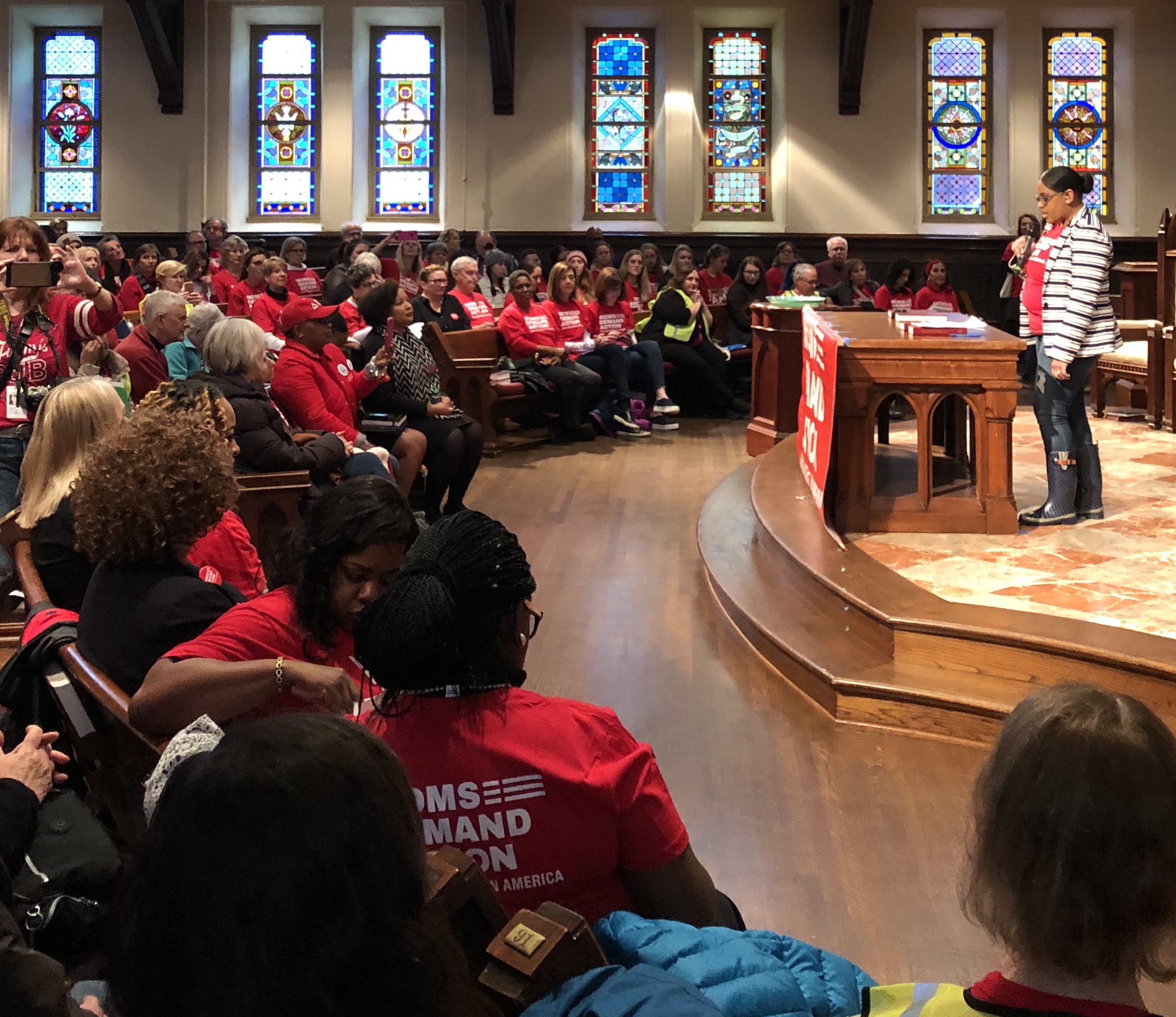 Image from Advocacy Day, a woman standing on a stage with a microphone as a crowd listens.