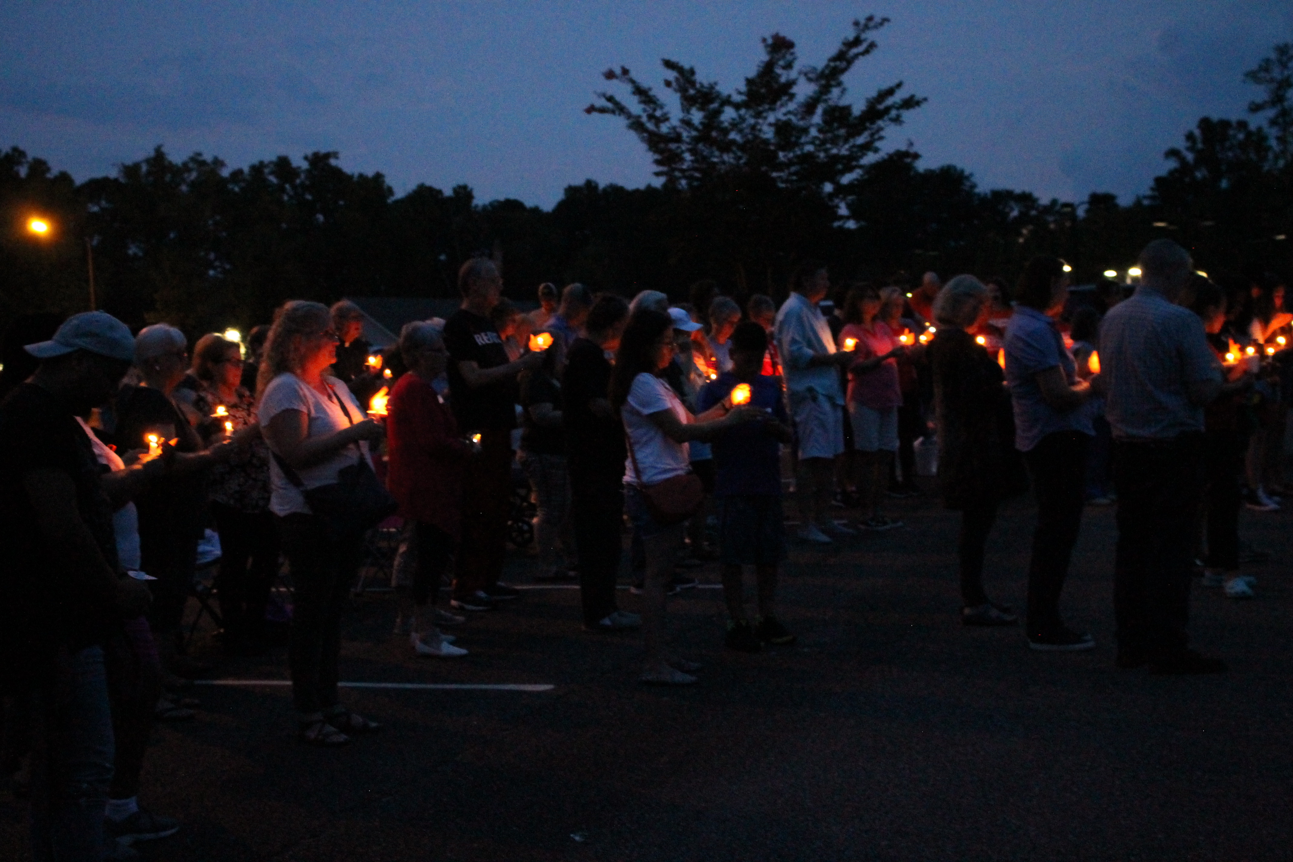 Image from a candlelight vigil, a crowd holding candles in the dark.